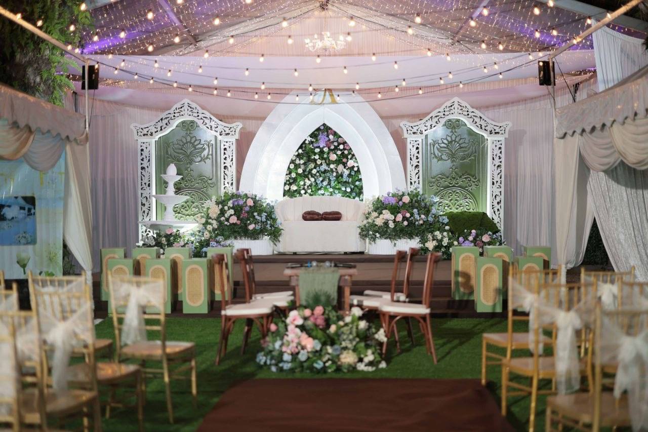 Pelamin putih berhias bunga dengan lampu kelip di bawah kanopi outdoor